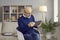 Serious senior man in glasses sitting in chair and using his modern digital tablet