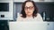 Serious senior woman in glasses working at home with a laptop