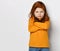 Serious small red haired girl in yellow comfortable longsleeve standing with crossed hands and frowning