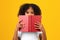 Serious smart curly teenager black schoolgirl in white t-shirt looks from behind book