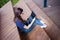 A serious student girl in glasses sits with legs on wooden steps, with an open laptop on her lap. Studying online.