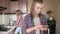 Serious stylish long-haired young man something prints on his smartphone in the kitchen. Behind his back is his wife or