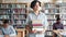 Serious teenage boy walking in library with bunch of books looking around