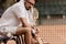 serious tennis player sitting on chair with tennis racket at court and looking