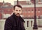 Serious thinking business man in fashion style coat sitting on the street and looking on autumn background. Portrait