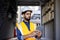 Serious thinking and focused engineer working in factory in hard hat and vest, man using tablet computer reading diagram