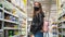 Serious tired woman in protecting mask in shop. A girl walks around grocery store. Pandemic N1H1 coronavirus, virus protection.