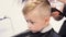 A serious toddler child on a haircut by a hairdresser.