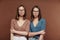 Serious twin sisters in pullovers and eyeglasses standing close to one another