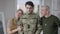 Serious unhappy young man in camouflage standing at home with proud father and mother looking at camera smiling