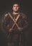 Serious viking with axes in a traditional warrior clothes, posing on a dark background.