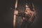 Serious viking woman with bow and arrow in a traditional warrior clothes, posing on a dark background.