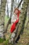 The serious woman with a red scarf costs having leaned against a birch in the wood