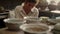 Serious woman scraping clay plate in pottery. Girl carving on product in studio