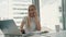 Serious woman working in light office room. Elegant modern business woman with laptop and papers at long table in