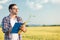 Serious young agronomist or farmer measuring wheat plant size in a field, writing data into a questionnaire