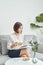 Serious young Asian girl in blouse and skirt.sitting on sofa and drinking tea while reading book in living room