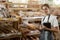 Serious young baker with tablet standing by display with fresh baked bread, smiling woman in supermarket bakery looking