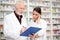 Serious young female and senior male pharmacists standing in front of shelves with medications in a drugstore