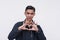 A serious young Filipino man making a hand heart gesture while trying to look cool. Isolated on a white background