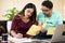 Serious young indian couple calculating expenses or monthly bills in front of laptop while sitting at home - concept of