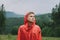 Serious young male tourist in a red raincoat stands in the mountains and looks away in concentration. Portrait of a beautiful man