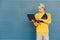 Serious young man in street clothes stands against the background of a blue wall and uses a laptop. Freelancer works on a notebook