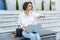 Serious young woman sitting on bench outdoors at the street, using laptop computer,