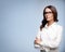 Seriously looking young brunette businesswoman in glasses, confident white clothing, over grey color background, with copy space