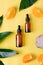 Serum bottles, orange fruit, palm leaf and stone on yellow