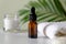 Serum or essential oil bottle with moisturizer and towel, palm leaf on the background. Clear amber glass dropper bottle with