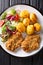 Serve fried steaks in sesame breading with new potatoes and fresh salad close-up on the table. Vertical top view