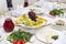 served festive dining table with dishes, white tablecloth, vegetables, fruits, drinks, salads, glasses