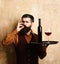 Service and catering concept. Man with beard holds wine on beige wall background