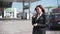 Service, satisfied female client drinks coffee at a gas station while car is fueled with gasoline, fuel prices