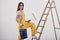 Services in repair. Beautiful brunette in yellow uniform and blue colored bucket stands near the ladder