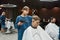 Serving client in barbershop. Professional young barber girl drying hair of a handsome guy, making trendy haircut. Focus