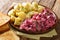 Serving herring salad with vegetables and a side dish of boiled potatoes close-up in a plate. horizontal