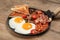 Serving pan with fried eggs, mushrooms, beans, bacon, tomatoes and toasted bread on wooden table, closeup. Traditional English