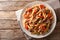 Serving penne pasta with pulled pork, cheese, tomato sauce and herbs close-up on a plate. horizontal top view