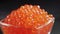 A serving of selected red caviar rotates on a black background in a transparent glass bowl. Gourmet seafood, gourmet