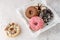 Set of assorted colorful white and dark chocolate glazed donuts with mix sprinkles on wooden tray closeup on stone table