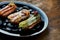 Set of assorted French custard eclairs with custard and assorted toppings served on a black plate on a wooden background.