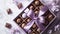 A set of chocolates in an open craft box, decorated with satin purple ribbon on a pastel purple background with flowers