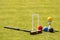 A set of colored balls, a hammer and a winners prize at the croquet wicket on the green lawn