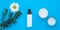 Set of cosmetic bottles, face cream and lotion on a blue background with a green branch and a daisy. Glass jar and spray with