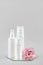 Set of cosmetic for skin care face, body or hair. White blank cosmetics bottles, tube and pink flower on mirror, gray background.