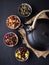 Set of different herbal and fruit dry teas in clay bowls,black clay teapot, dark moody, stone,concrete background