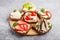 Set of different sandwiches with cheese, radish, lettuce, strawberry, sprats, tomatoes and cucumber on wooden board on a gray