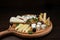 Set of European cheeses on a wooden table in the restaurant. The dish is decorated with walnuts, grapes and greens. Tasty snack.